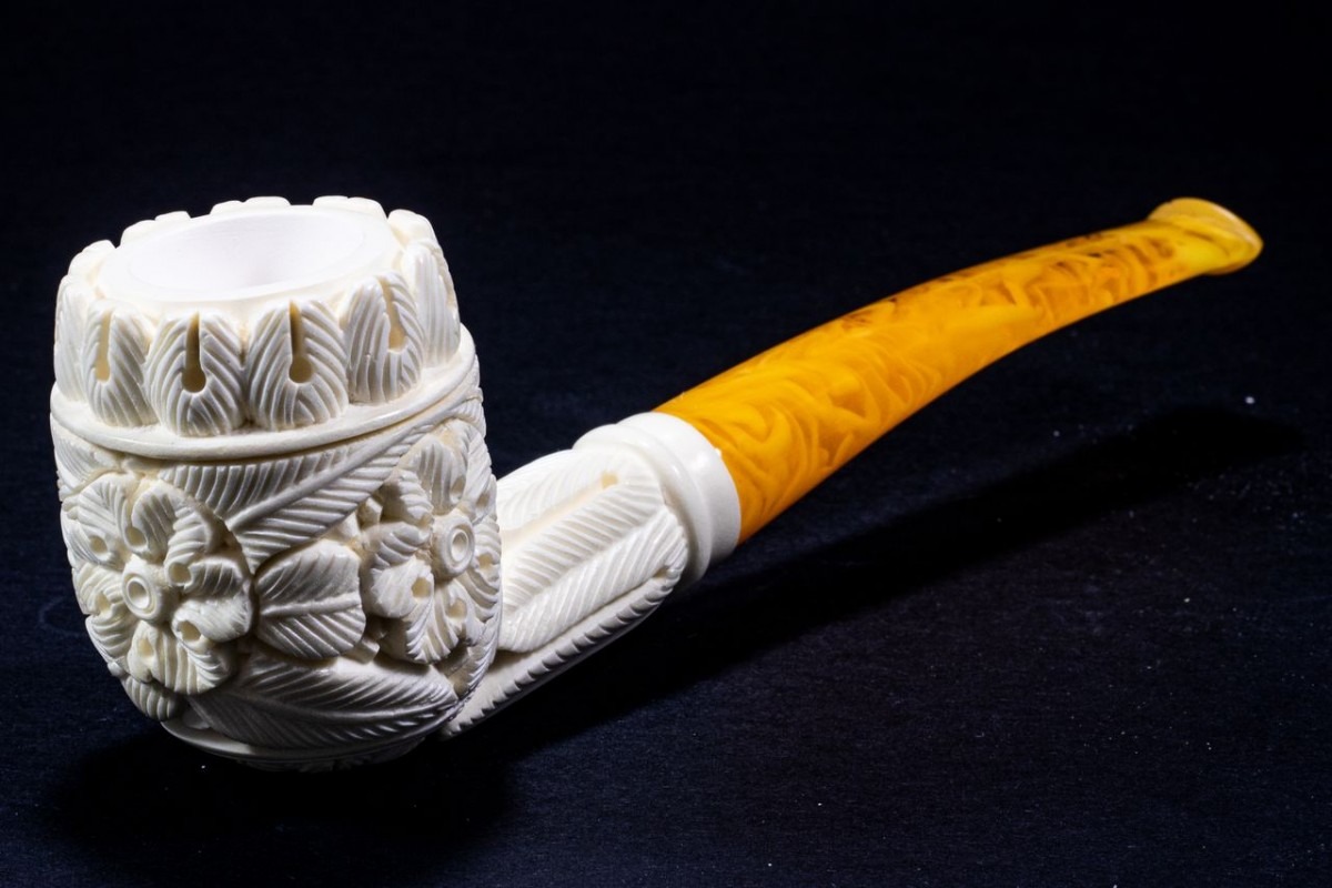 Decorative Meerschaum Quarter Bent Billiard pipe featuring detailed floral carvings on the white bowl and a polished amber-toned stem, displayed on a dark surface.